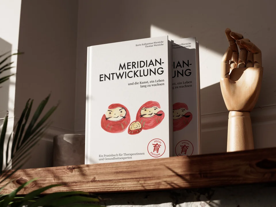 Buch „Meridian-Entwicklung und die Kunst, ein Leben lang zu wachsen“ von Karin Kalbantner-Wernicke und Thomas Wernicke auf einem Holzregal, daneben eine Holzhand