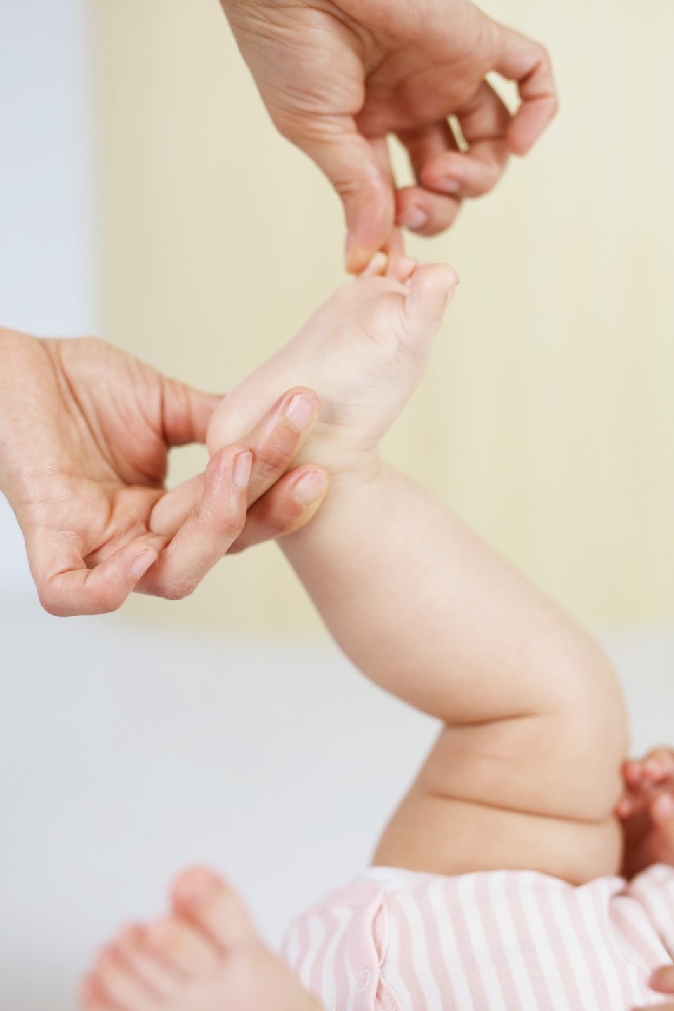 Ein Erwachsener führt eine sanfte Shiatsu-Massage an den Armen und Händen eines Babys durch, das rosa-weiß gestreifte Kleidung trägt.