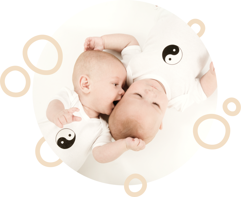 Zwei Babys liegen auf weißem Hintergrund und schauen sich an, umgeben von beige Symbolen wie Yin-Yang-Zeichen und Kreisen, die Harmonie und Ganzheitlichkeit darstellen.