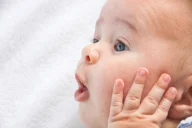 Baby mit blauen Augen, das eine Hand an die Wange legt und den Mund zu einem kleinen "O" formt