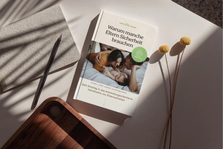 Ein aufgeschlagenes Buch mit dem Titel "Warum manche Eltern früher Betreuung brauchen" liegt auf weißem Untergrund neben getrockneten Gräsern und schwarzen Stiften. Das Buch zeigt auf dem Cover ein Foto von Erwachsenen und Kindern. Ein grüner Kreis mit Text befindet sich auf der Buchseite.