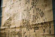 Historisches Dokument oder Diagramm mit östlichen Schriftzeichen zeigt ein menschliches Körpersystem mit beschrifteten Meridianlinien und Akupunkturpunkten. Das vergilbte, alte Papier enthält handschriftliche Notizen und Zeichnungen zur Darstellung der Energiebahnen im traditionellen Heilsystem.