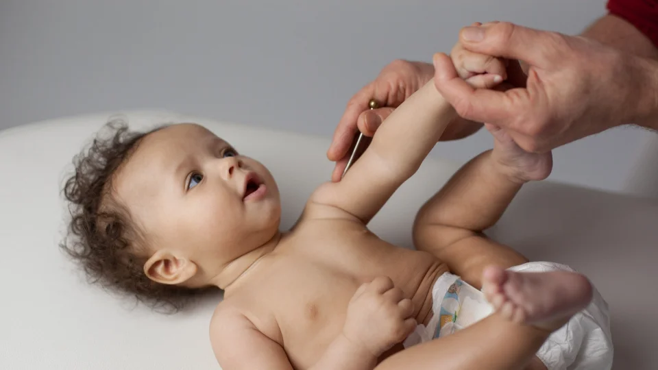 Ein kleines Kind liegt auf dem Rücken auf einer weißen Oberfläche, während ein Erwachsener mit den Fingern sanft auf die Brust des Kindes drückt. Das Kind schaut nach oben und wirkt entspannt während der Behandlung.