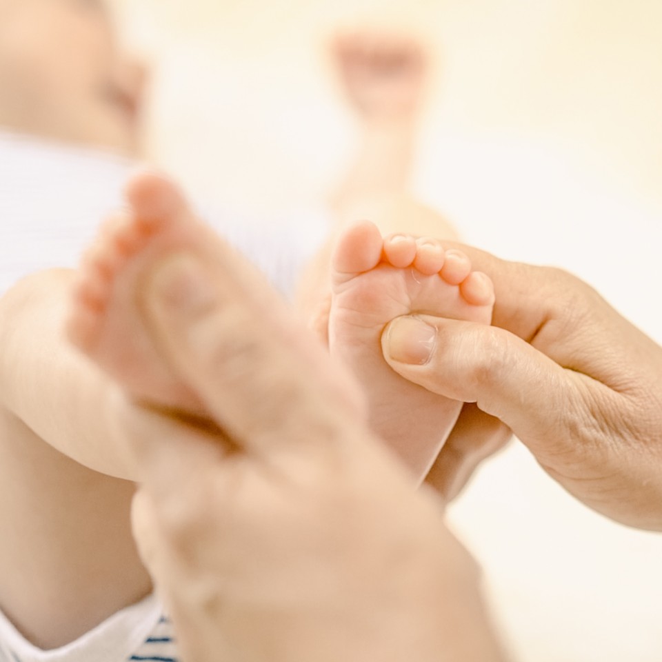 Ein Erwachsener hält die kleine Hand eines Babys. Die zarte Berührung zeigt eine liebevolle Verbindung zwischen Betreuer und Neugeborenem.