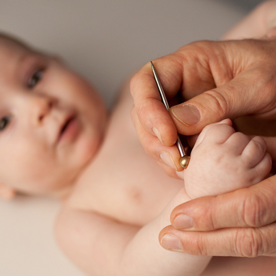 Ein Erwachsener führt eine sanfte Shonishin-Behandlung an einem Säugling durch, wobei ein spezialisiertes Behandlungsinstrument auf der Haut des Babys angewendet wird. Das Baby liegt entspannt im Hintergrund, während die Behandlung durchgeführt wird.